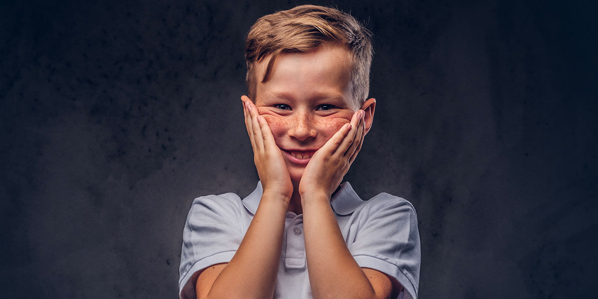 Foto raffigurante un ragazzino sorridente con le mani in faccia